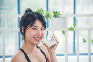 Women hands holding white glass of milk pouring from bottle. Asian women smile laugh look at camera...