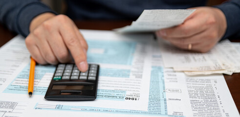 A man organizing individual income tax return form 1040 and receipts. Blurred background. Tax...