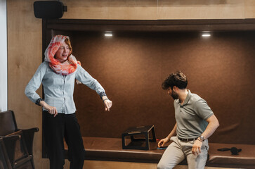 Muslim woman having fun during office break hours with her coworker who is sitting in a recessed sofa area