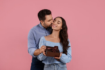 Man kissing his smiling girlfriend on pink background. Celebrating holiday