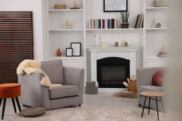 Comfortable armchairs, fireplace and shelves in living room. Interior design