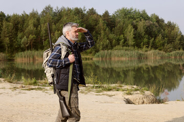 Man with hunting rifle near lake outdoors. Space for text