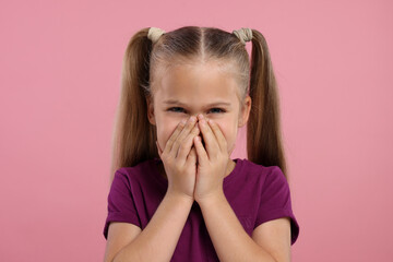 Embarrassed little girl covering her mouth with hands on pink background