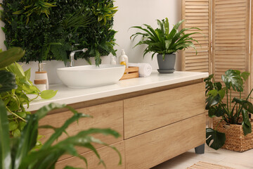 Green artificial plants, vanity and different personal care products in bathroom