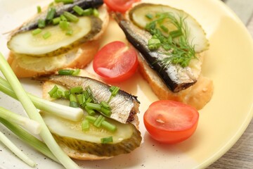 Delicious sandwiches with sprats, pickled cucumber and green onion served with tomato on wooden table, closeup
