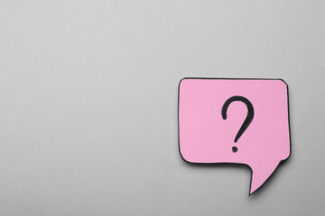 Paper speech bubble with question mark on light grey background, top view. Space for text