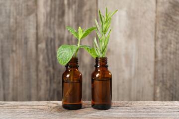 Bottles with essential oils, mint and rosemary on wooden table