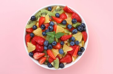 Yummy fruit salad in bowl on pink background, top view
