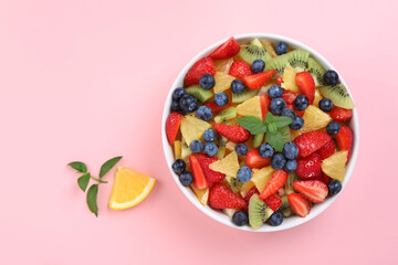 Yummy fruit salad in bowl on pink background, top view. Space for text