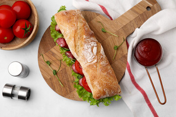 Delicious sandwich with sausages, vegetables and ingredients on white table, flat lay