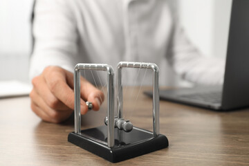 Man playing with Newton's cradle at office table, closeup. Physics law of energy conservation