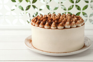 Delicious tiramisu cake with cocoa powder on white wooden table, closeup