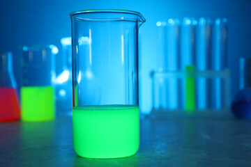 Laboratory beaker with luminous liquid on table against blurred background, closeup