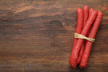 Many thin dry smoked sausages on wooden table, top view. Space for text