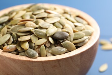 Wooden bowl with peeled pumpkin seeds on table, closeup