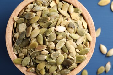 Bowl with peeled pumpkin seeds on blue wooden table, top view
