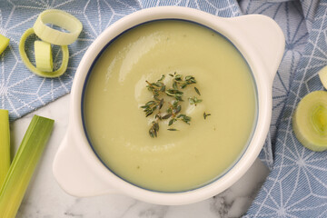 Tasty leek soup in bowl on white marble table, flat lay