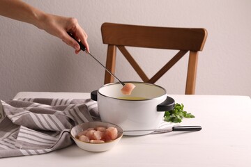 Woman dipping piece of raw meat into oil in fondue pot at white wooden table, closeup