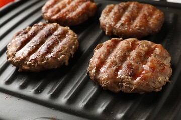 Delicious hamburger patties cooking on electric grill, closeup