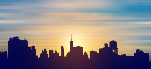 New York City downtown skyline buildings silhouetted against the colorful sky with the light of...