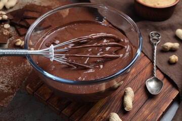 Bowl of chocolate cream, whisk and spoon on table, closeup