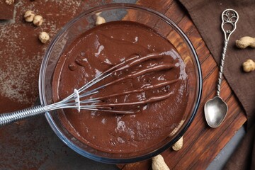 Bowl of chocolate cream, whisk and spoon on table, above view