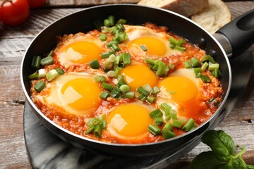 Delicious Shakshuka in frying pan on wooden table, closeup