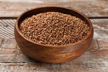 Bowl with dry buckwheat on wooden table, closeup