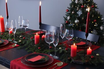 Elegant Christmas table setting with dishware and burning candles in festively decorated room