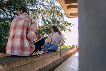 Girls were distracted by something while writing homework. They are sitting on a wall 