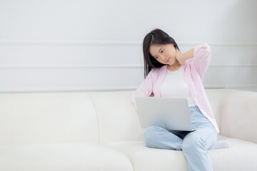 Obraz na płótnie Canvas Beautiful young asian businesswoman sitting on sofa and working from home and break while stretch muscle neck for relax in living room at home, woman is freelance working on laptop, business concept.