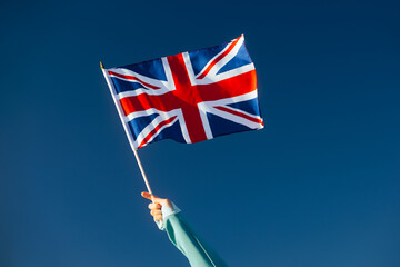 Hand Waiving a Union Flag on a Blue Sky . Cheerful enthusiastic patriotic person displaying the...