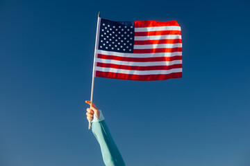 Hand Waiving an American Flag on a Blue Sky. Cheerful enthusiastic patriotic person displaying the...