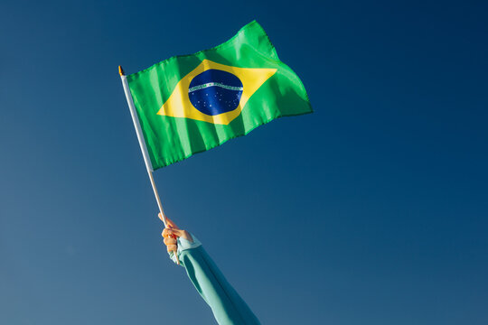 Hand Waiving a Brazilian Flag on a Blue Sky. Cheerful enthusiastic patriotic person displaying the symbol of Brazil
