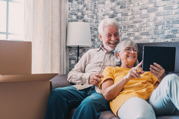 Happy retired senior family couple relaxing on sofa after moving activities, sharing tablet computer, looking at screen, laughing, making video call, using online app, Internet service.