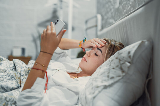 Top view unhappy woman feeling headache after sudden awakening by phone call, message signal or alarm in early morning, exhausted young female suffering from insomnia or migraine, lying in bed.