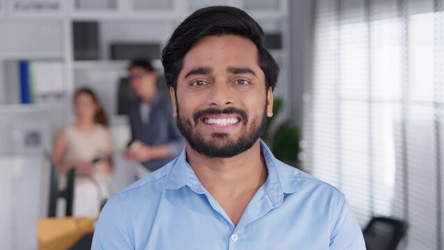 Portrait of formal business man confident successful. Indian businessman or manager in light blue shirt, stands at workplace in office, arms crossed, looks directly at camera and smiles friendly