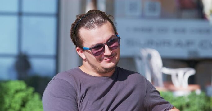 Portrait of young attractive self-confident man in sunglasses, sitting on street flirting with passers-by, pestering women, making compliments with gestures Harassment pick-up womanizer Sexual freedom