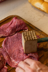a photograph with raw meat cut into steaks to make cordovan tenderloins with a knife and a close-up of a hand cleaning or tenderizing the meat