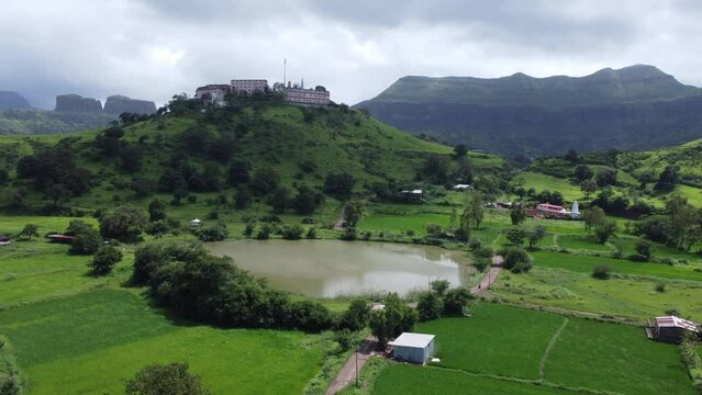 Aerial view of Nil Parvat sacred temple on the edges of Brahmagiri hills with the view of Trimbakeshwar town and Sahyadri mountains under an overcast sky in monsoon, Nashik, Maharashtra, India