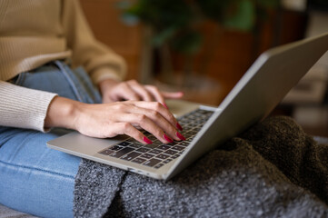 Close-up image of a woman typing on keyboard, using her laptop while relaxing at home.