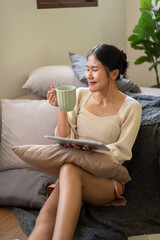 A relaxing and happy Asian woman enjoying her morning coffee in her bedroom. Domestic life