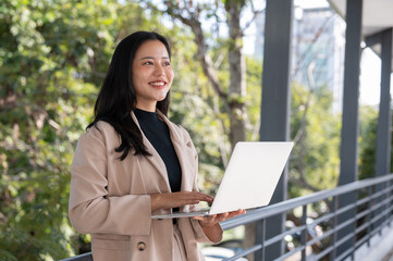 An attractive millennial Asian businesswoman working on her laptop on a skywalk in the city.