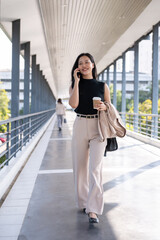 Naklejka premium A confident and busy Asian businesswoman is talking on the phone while going to her office.
