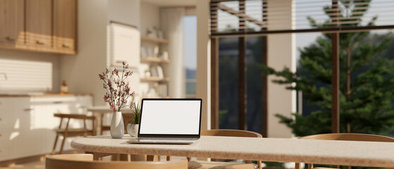 A laptop mockup on a dining table in a beautiful Scandinavian kitchen in a modern spacious home. - obrazy, fototapety, plakaty