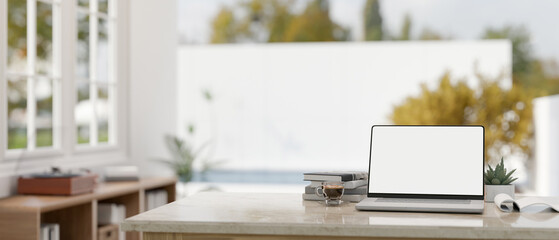 Home workspace, a white-screen laptop mockup on a table in a modern white room.