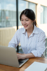 An attractive Asian businesswoman is working on her laptop in a modern office or co-working space.