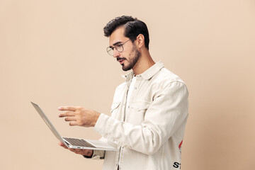 Portrait of a stylish man pensive look in glasses with a laptop in the hands of a freelancer, on a beige background in a white t-shirt, fashionable clothing style, space space