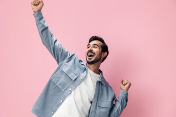 Fashion portrait of a brunette man with beard happiness open mouth victory raised his hands with his fist up on a pink background in a white T-shirt smile and joyful emotion on his face, copy space - Powered by Adobe