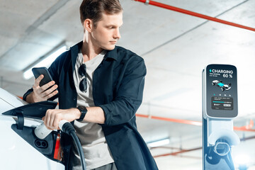 Young man travel with EV electric car to shopping center parking lot charging in downtown city...